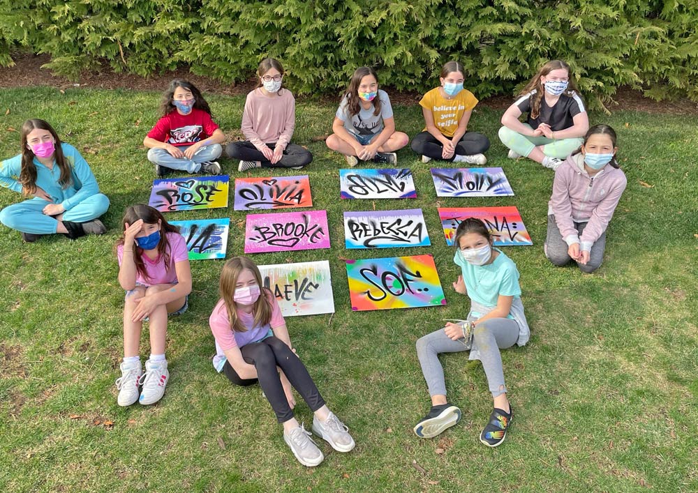 Kids sitting on grass together with small canvas artworks