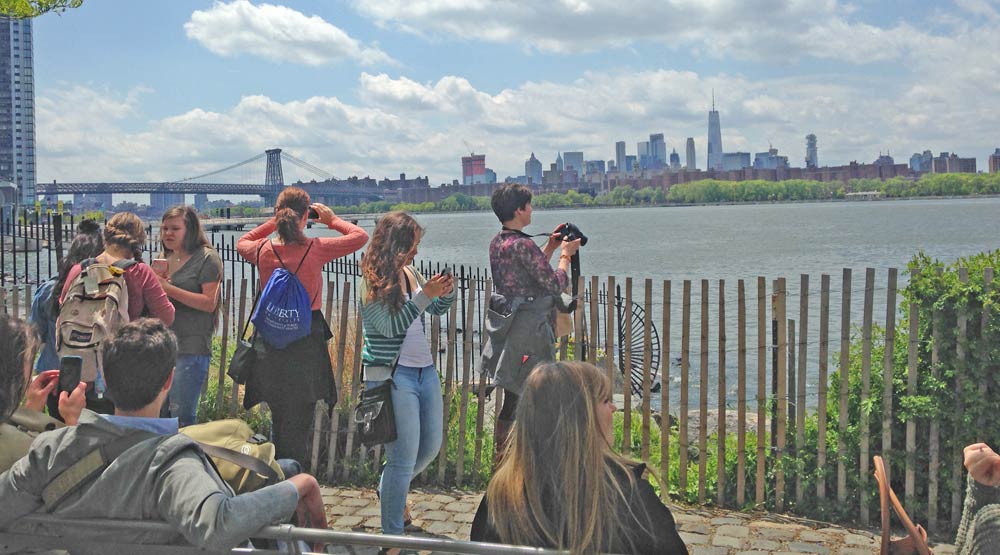 people by East River taking photos of Manhattan skyline