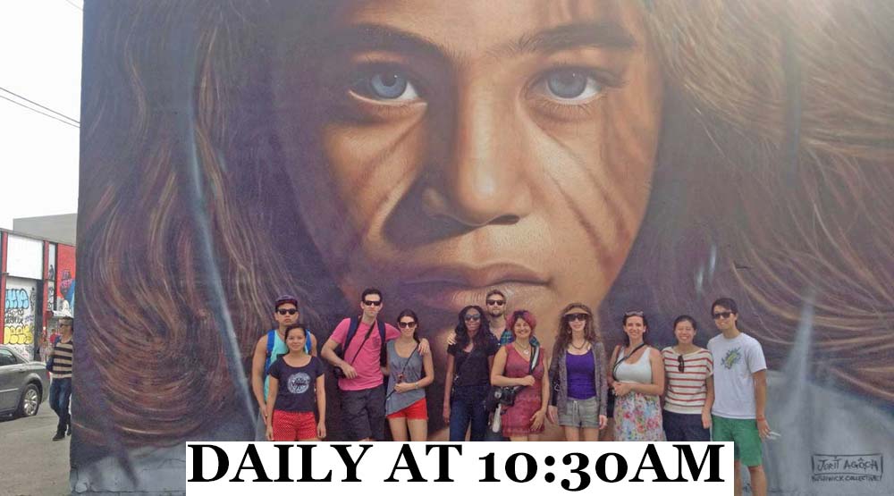 Tour group stands in front of graffiti portrait mural of young girl.